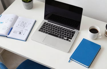 A top-down view of a modern desk in a North American home office featuring a laptop, a notebook with diagrams, and a cup of coffee. The lighting is crisp and intelligent, using a color palette of Sky White and Bright Blue.