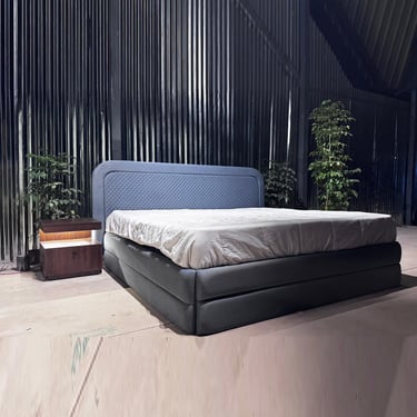 Modern upholstered bed frame with a quilted headboard and lighted wooden nightstand in a studio.