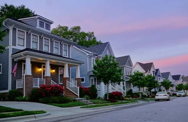 Modern luxury suburban homes on a quiet street at sunset with purple skies and manicured lawns.