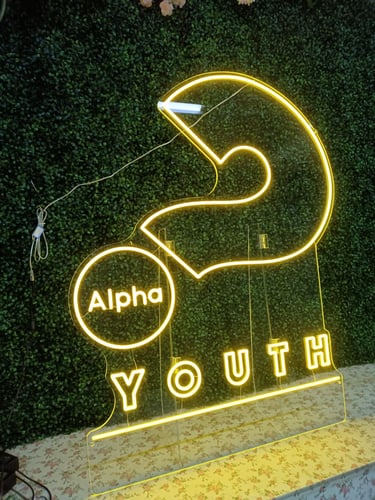 Gelbes LED Neon Logo mit Schriftzug „Alpha Youth“ auf dunklem Hintergrund