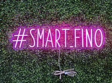 pinkes LED Neon Schild mit Schriftzug „#SMART_FINO“ auf grüner Pflanzenwand