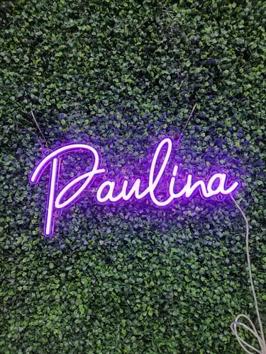 lila LED Neon Schild mit Schriftzug „Paulina“ auf grüner Pflanzenwand