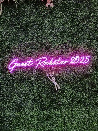 pinkes LED Neon Schild mit Schriftzug „Guest Rockstar 2025“ auf grüner Pflanzenwand bei Hotel Event