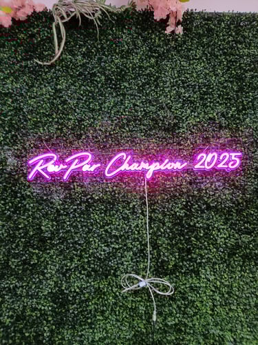 pinkes LED Neon Schild mit Schriftzug „Rockstar Champion 2025“ auf grüner Pflanzenwand bei Event