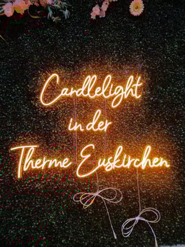 oranges LED Neon Schild mit Schriftzug „Candlelight in der Therme Euskirchen“ auf grüner Pflanzenwand