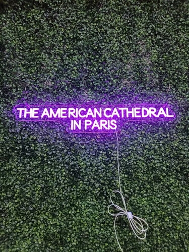 lila LED Neon Schriftzug „The American Cathedral in Paris“ Neon Logo Schild auf grüner Pflanzenwand