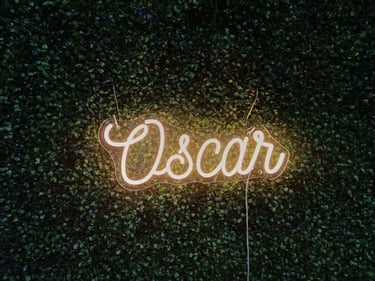 Warm weißes Neon Schild „Oscar“ personalisierter LED Neon Schriftzug Name auf grüner Pflanzenwand