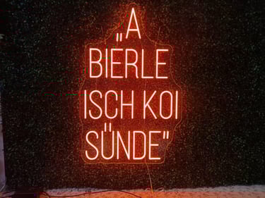 oranges Neon Schild „A Bierle isch koi Sünde“ LED Neon Spruch Schild auf Grünem Hintergrund