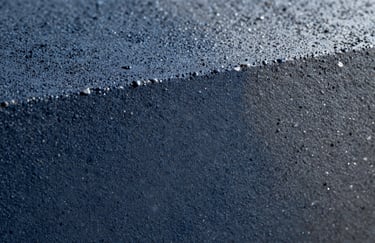 A macro photograph showing the intricate texture of polished concrete. Small aggregates are visible within the Deep Navy Blue and Steel Grey matrix, showcasing a high-gloss, professional finish.