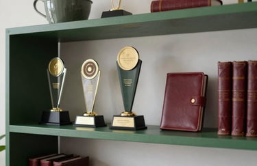 A crisp photograph of a minimalist North American office shelf holding professional award trophies and leather-bound journals. Matte Forest Green and Deep Ripe Crimson elements are subtly visible in the decor.