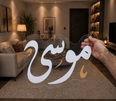 لوحة أكريليك شفافة باسم موسى مكتوبة بخط عربي أنيق باللونين الأبيض والذهبي، تُحمل باليد في غرفة معيشة