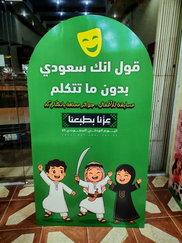 لوحة إعلانية خضراء لفعالية مسابقة للأطفال بمناسبة اليوم الوطني السعودي 95 تظهر رسومات كرتونية لأطفال