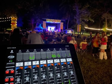 A Midas M32 mixing console app on a tablet used for remote live sound control at an outdoor night concert.
