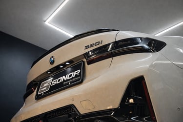 Rear view of a white BMW 320i featuring a Sonor performance exhaust system and carbon fiber spoiler.