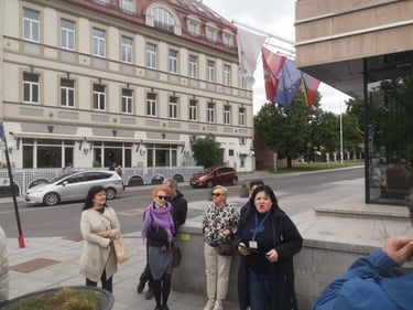 Gidė Ramutė veda ekskursiją Vilniaus senamiestyje grupei turistų prie viešbučio ir vėliavų.