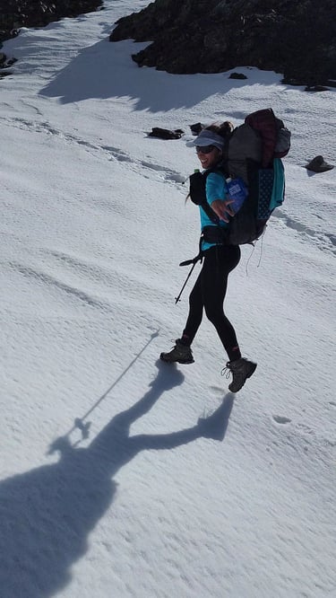 Female hiker with a backpack and ultralight ge and trekking poles walking on a snowy mountain trail.