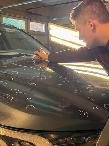 Professional PDR tech marking with a white marker the hail damage on the hood of a car.