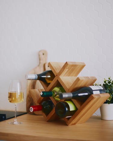 Oak wine rack filled with bottles on a table, accompanied by an elegant glass of white wine