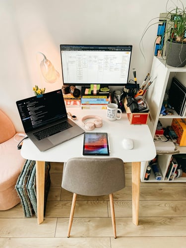 Modern home office setup with a laptop, monitor, tablet, and pink headphones on a white desk.