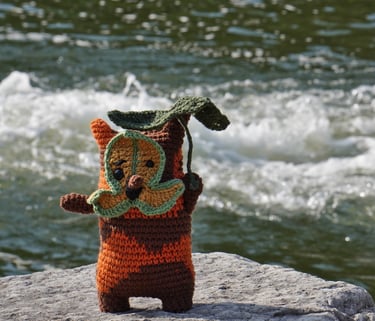 A korok holding a leaf standing on a rock in front of a stream.