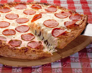 Pizza resting on a Checkerboard tablecloth showing a slice being removed with cheese dripping.