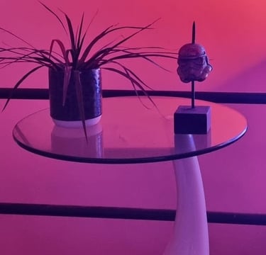 Sculpture contemporaine en métal représentant une tête stylisée sur socle noir, posée sur table en verre avec plante