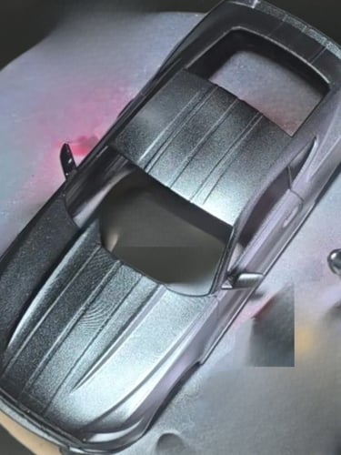 Aerial view of a model car being spray painted with metallic silver and black paint.