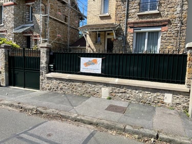 Stone house front with scaffolding and a black iron fence featuring a painting contractor sign.