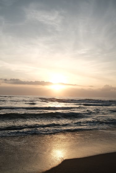 Golden sunrise over ocean waves on a sandy beach under a cloudy sky.