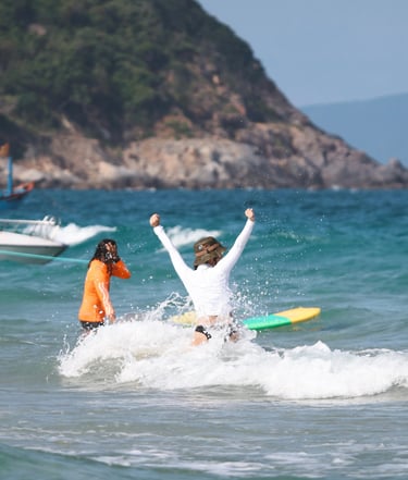 A person celebrates catching a wave while surfing at a tropical beach with rocky hills.
