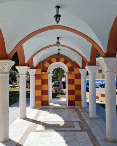 White marble colonnade with arched ceilings and striped stone pillars in a Mediterranean courtyard.