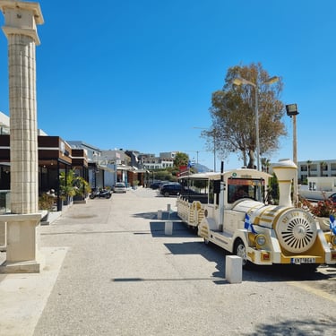 White and gold tourist fun train parked on a sunny street in a Greek seaside resort town.