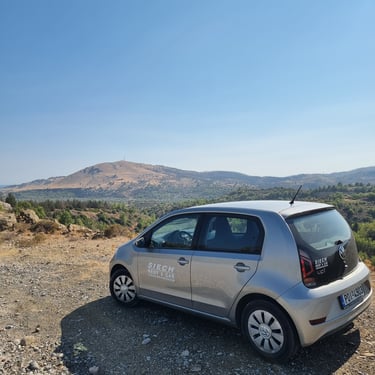 Silver Volkswagen Up rental car parked on a mountain overlook with scenic valley views.