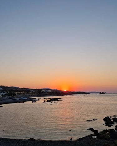 Sunset over a coastal village with fishing boats and a rocky shoreline at dusk.