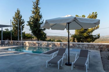 Luxury poolside patio with lounge chairs and white umbrella overlooking a scenic valley landscape.