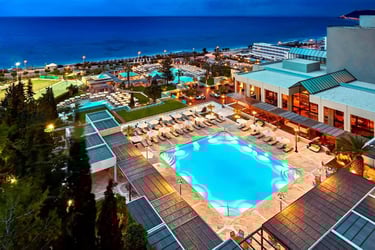 Luxury beach resort at dusk with illuminated swimming pools, tennis courts, and ocean views.