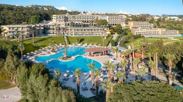 Aerial view of a luxury Mediterranean resort with large swimming pools, palm trees, and modern hotel buildings.
