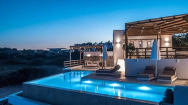 Luxury villa terrace with a glowing infinity pool and lounge chairs at twilight.
