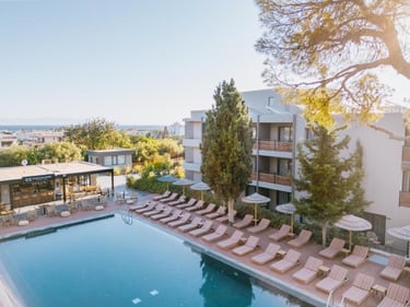 Luxury hotel swimming pool with lounge chairs and straw umbrellas at a Greek seaside resort.