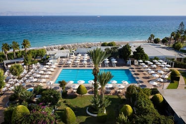 Aerial view of a luxury beachfront resort with a swimming pool, white umbrellas, and palm trees.