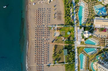 Aerial view of a luxury beachfront resort featuring swimming pools, sandy beach with umbrellas, and turquoise ocean water.