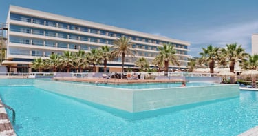 Luxury beach resort with a large outdoor swimming pool and palm trees under a clear blue sky.