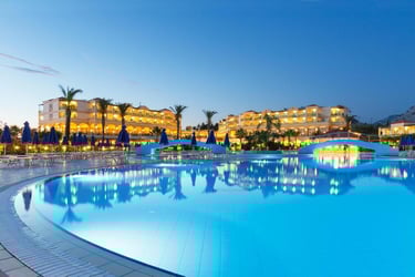 Luxury resort swimming pool at night with palm trees and illuminated hotel buildings.