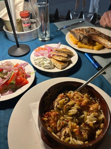 Authentic Greek dinner featuring beef giouvetsi with orzo pasta, fresh Greek salad, and pita bread with tzatziki.