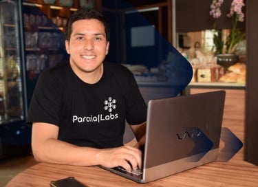 Douglas Silva, homem sorrindo, com camiseta preta, em uma cafeteria, sentado com seu notebook
