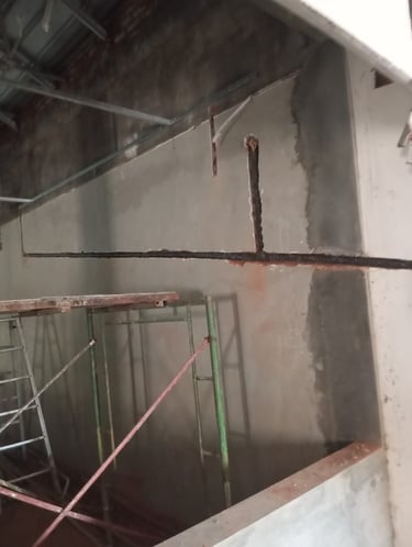 Interior wall under construction with electrical conduit grooves and green scaffolding.