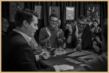 Maxwell Pritchard, seated at a table, performs magic for applauding audience members.