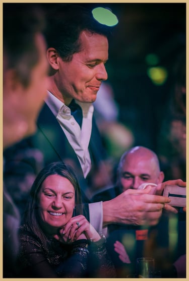 Maxwell Pritchard performs magic as audience members look on, grinning.