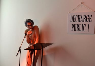 David nu au micro à côté de la pancarte : "Décharge public !" | Les Camps de l'Amor | David Noir | Photo Karine Lhémon