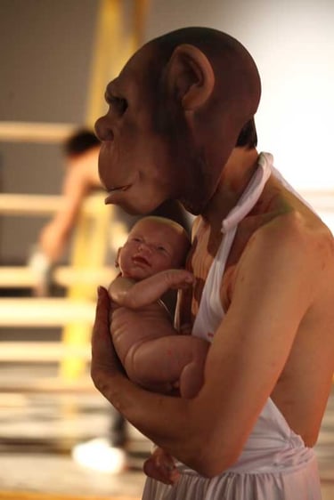 David Noir en robe et masque de guenon et un bébé dans ses bras | Permission refusée | David Noir | Photo Bernard Bousquet